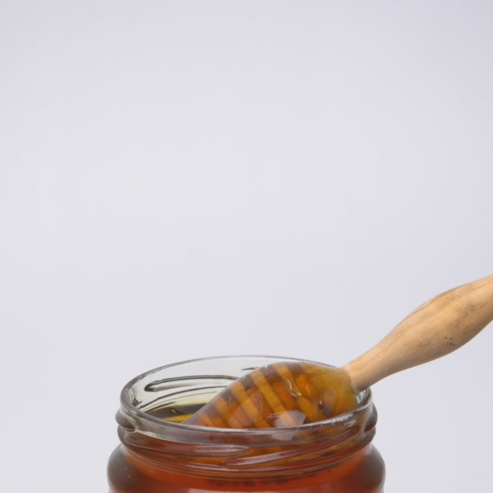 video of wooden honey dipper pouring into an open jar of thyme honey.