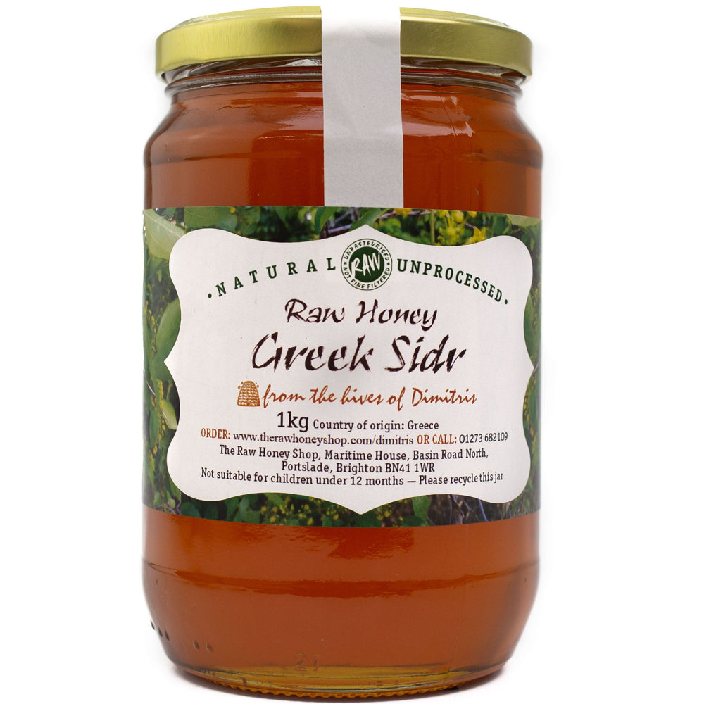 A jar of Greek Sidr honey from The Raw Honey Shop, with a label indicating it is raw, unprocessed, and comes in a 1kg size. The honey appears to have a deep golden color.