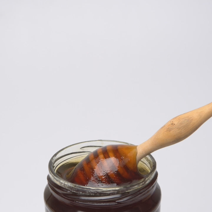 video of wooden honey dipper  dripping into an open jar of organic multifloral honey