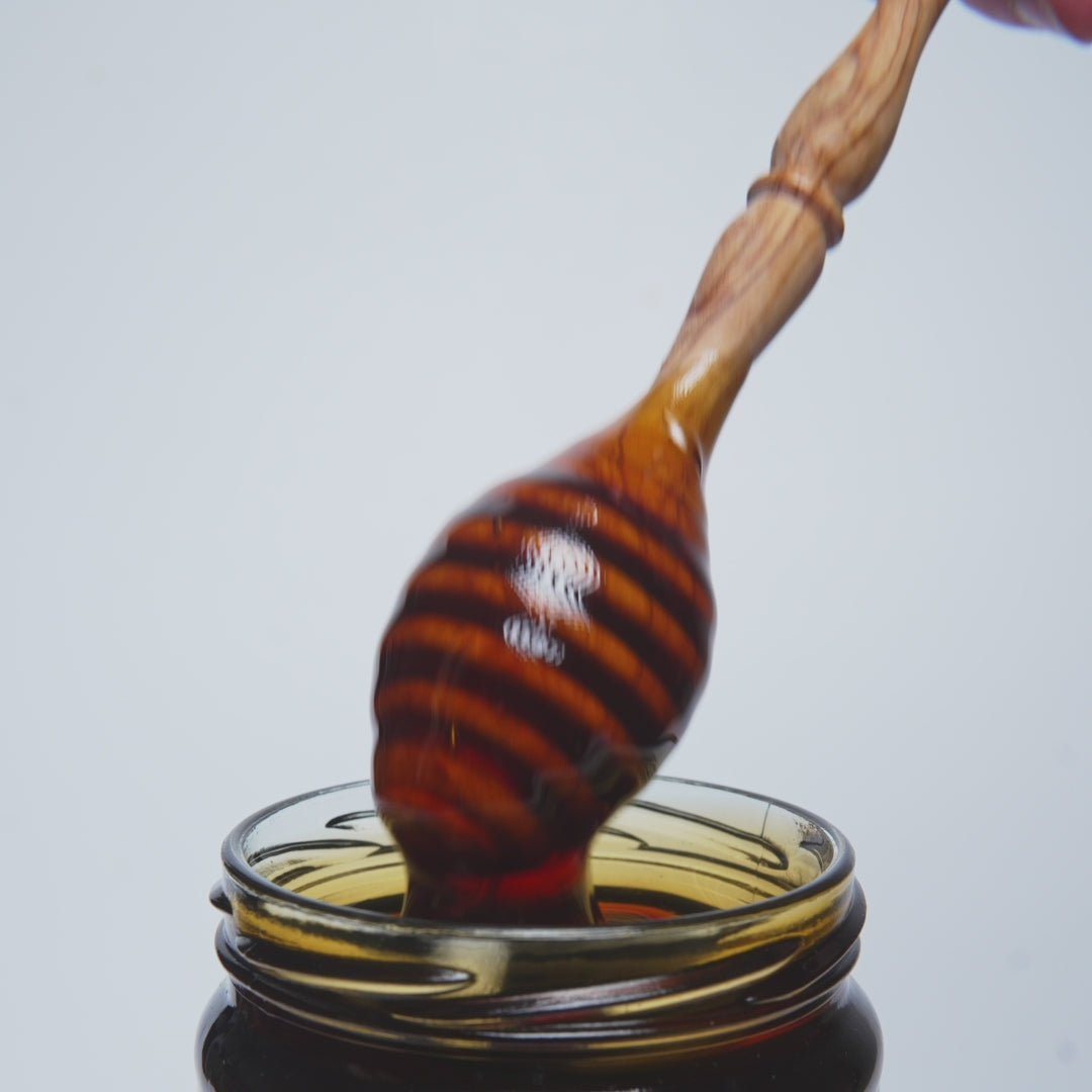 video of wooden honey dipper pouring into an open jar of heather honey.