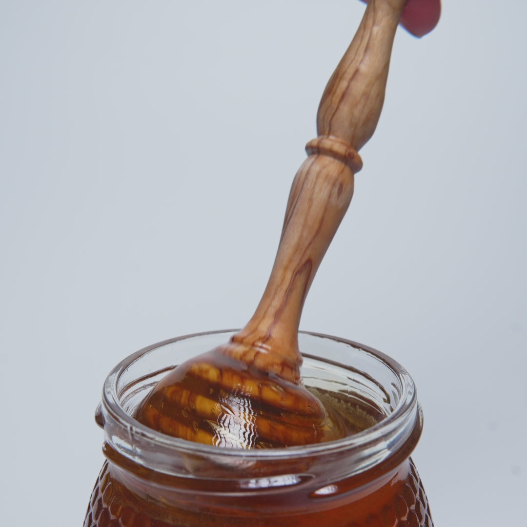 video of wooden honey dipper pouring into an open jar of rosemary honey.