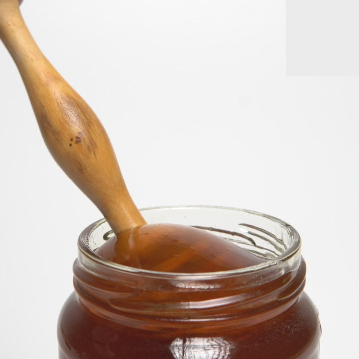 video of wooden honey dipper  dripping into an open jar of raw  organic Greek orange blossom honey